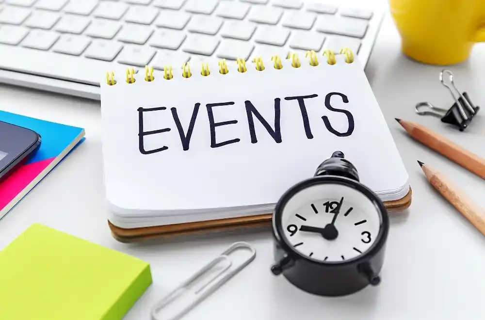 Events calendar on a white desk alongside a laptop, pen, pencil, coffee cup, and various office supplies.