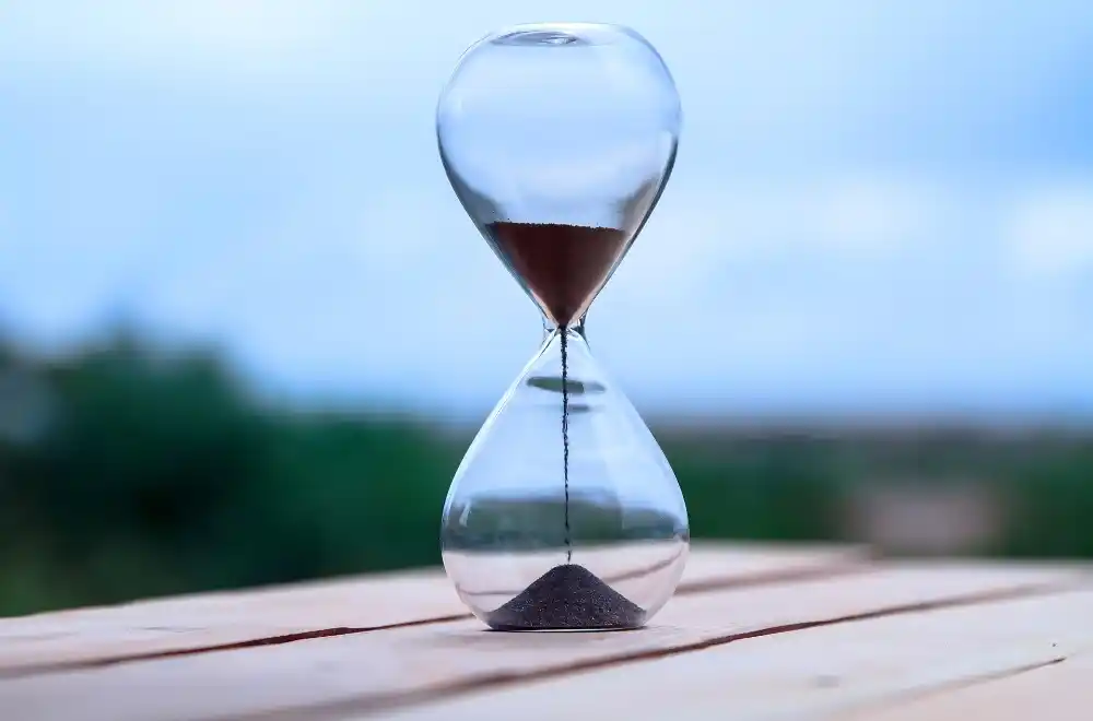 An hourglass placed elegantly on a wooden table, showcasing the flowing sand within its glass structure.